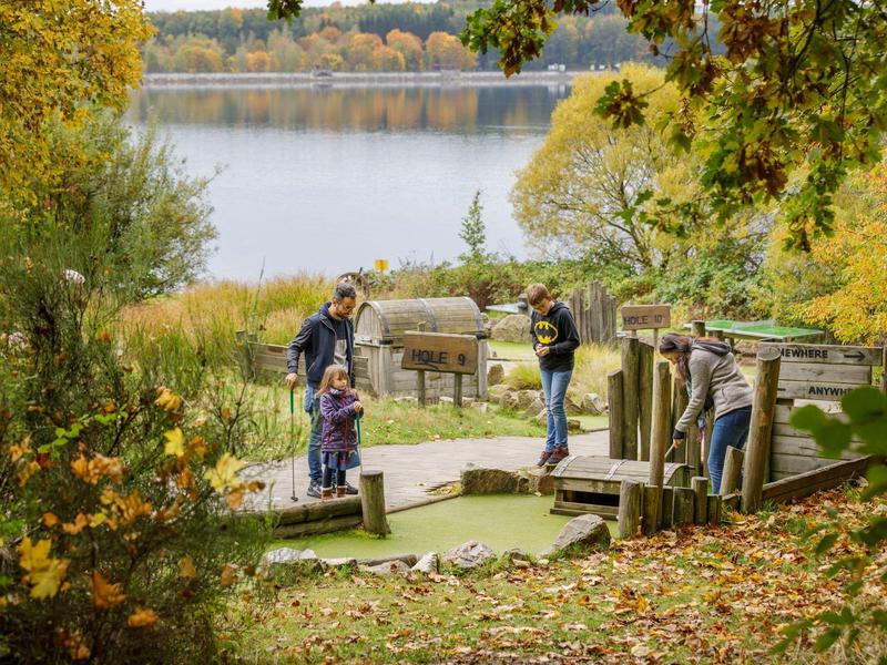 Personas juegan minigolf en un entorno otoñal cerca de un lago con hojas coloridas.