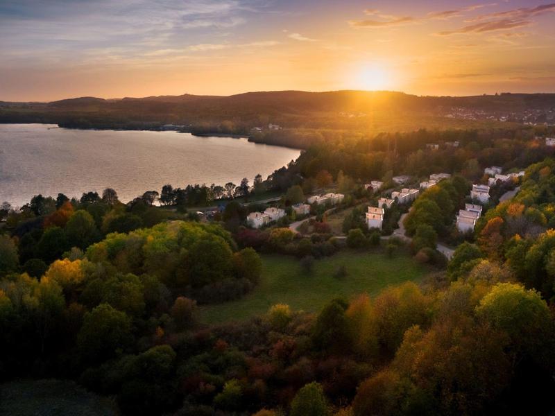 Atardecer sobre un lago arbolado y casas circundantes.