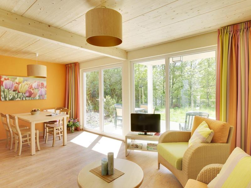 Sala luminosa con pared amarilla, asientos y gran ventana con vista al área verde.