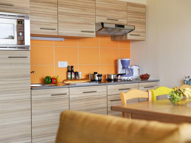 Cocina moderna de vacaciones con armarios de madera, salpicadero naranja y área de comedor en primer plano.
