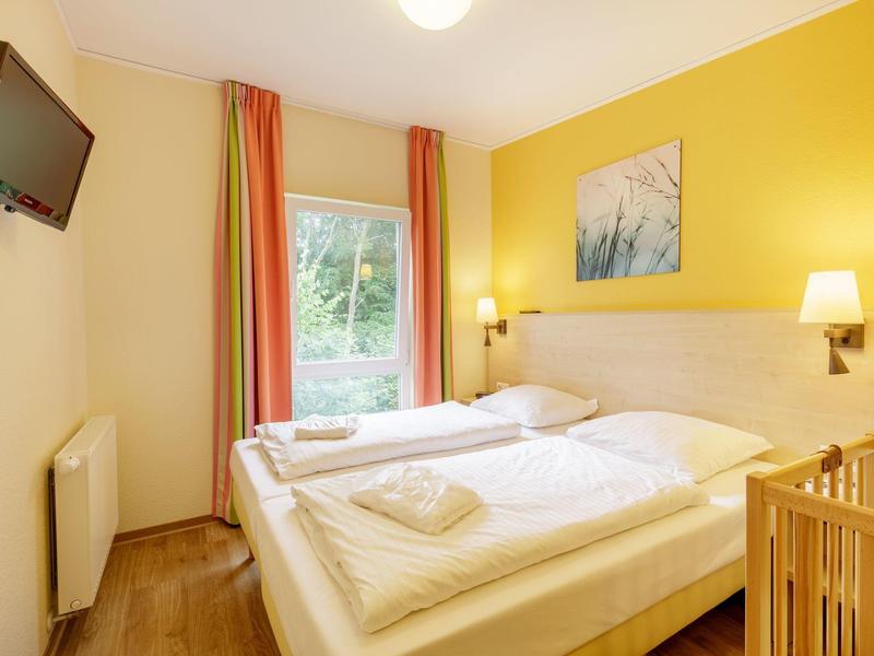 Habitación de hotel luminosa con cama doble, cortinas coloridas y suelo de madera junto a ventana con vista verde.