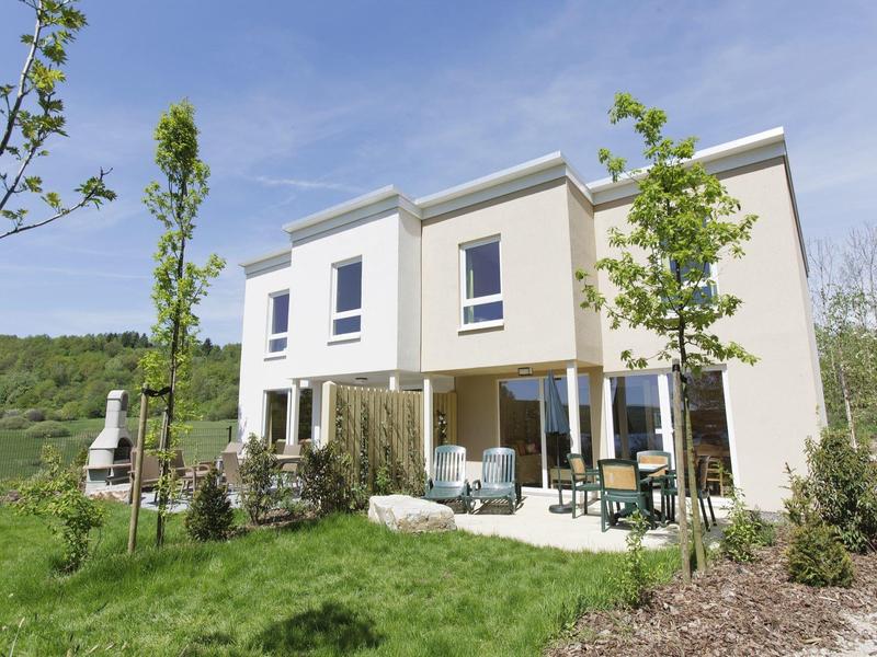 Casa de vacaciones moderna de dos pisos con terraza, jardín y entorno natural bajo cielo azul.