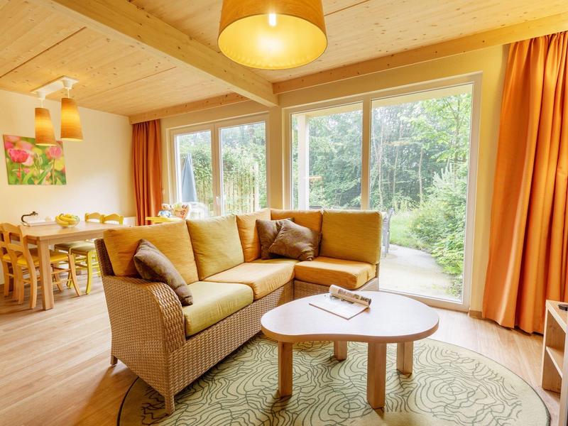 Sala luminosa con sofá marrón, mesa y grandes ventanas con vista al verde.