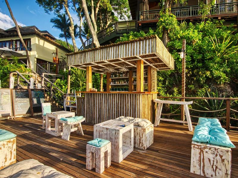 Bar all'aperto rustica con sgabelli in legno e vegetazione verde rigogliosa sullo sfondo.