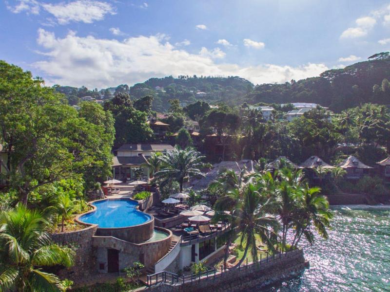 Una piscina d'hotel tropicale con palme e colline verdi sotto un cielo soleggiato.