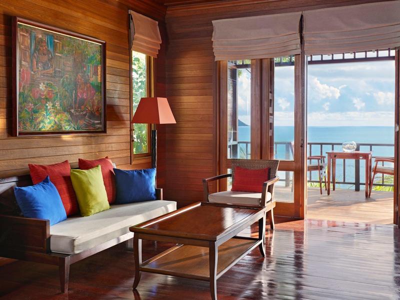 Accogliente soggiorno in legno con cuscini colorati e vista su terrazza e mare.