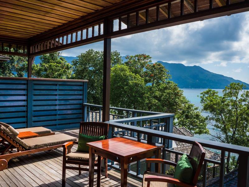 Balcone con tavolo, sedie e lettini con vista su montagne e lago sotto cielo nuvoloso.