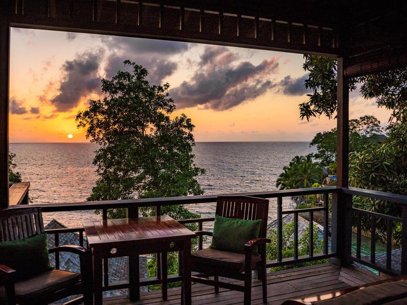 Balcone con sedie e tavolo con vista sul mare e tramonto con alberi.