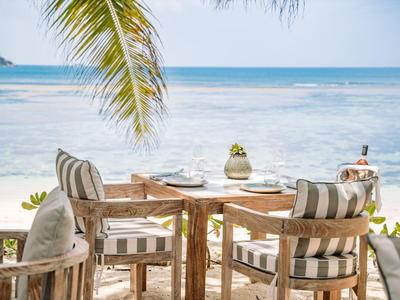 Terrasse mit Holztisch und Stühlen am Strand mit Blick auf das Meer unter Palmen