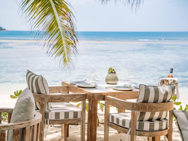 Terrasse de plage confortable avec table en bois et chaises rayées sous les palmiers au bord de la mer.