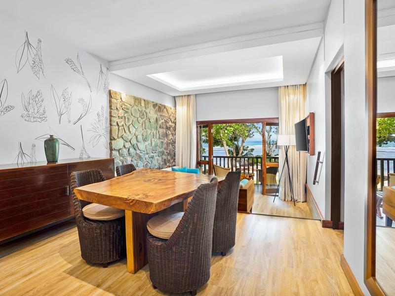 Salle à manger moderne avec table et chaises, accès au balcon avec vue sur la mer dans la chambre d'hôtel.