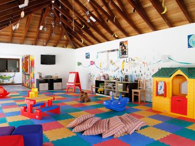 Salle de jeux pour enfants lumineuse avec tapis en mousse colorés, jouets et petite maison de jeu sous un plafond en bois.