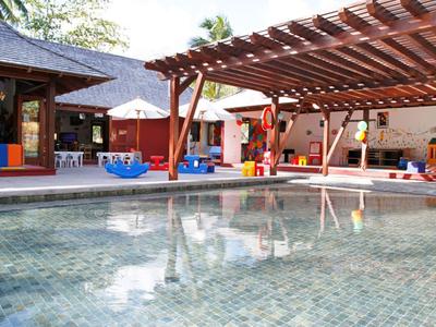 Piscine extérieure avec espace ombragé et jeux colorés pour enfants à proximité.