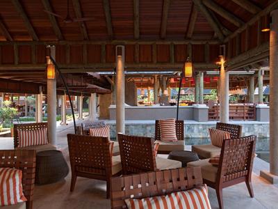 Espace lounge en plein air avec fauteuils en osier et tables sous un toit en bois.