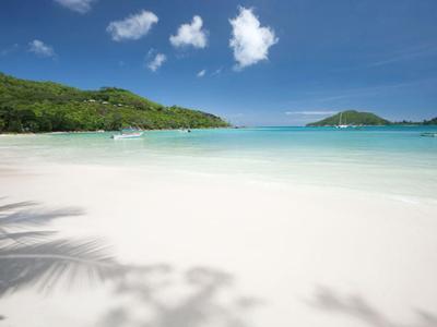 Plage de sable blanc immaculé avec eau turquoise claire et collines vertes sous un ciel bleu.