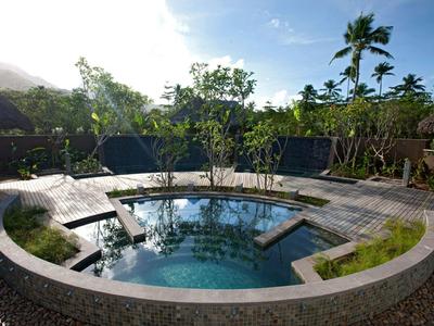Piscine ronde à l'eau claire entourée d'arbres et d'une terrasse en bois sous un ciel bleu.