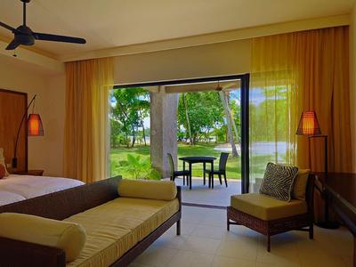 Chambre d'hôtel avec grand lit, coin salon et vue sur le jardin à travers des portes vitrées