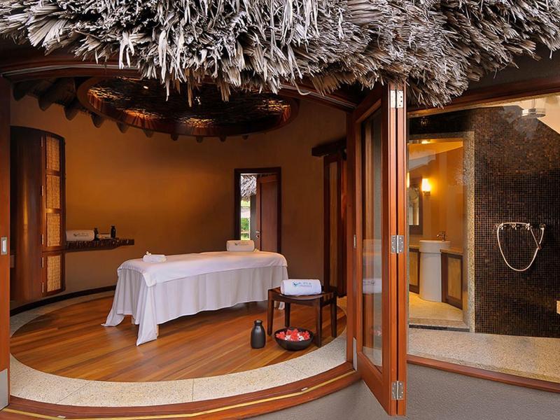 Salle de spa confortable avec table de massage, planchers en bois et plafond en chaume.