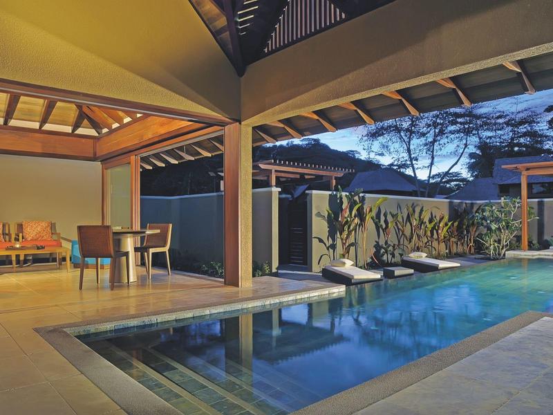 Piscine extérieure moderne avec chaises longues et espace assis ouvert sous un toit en bois.