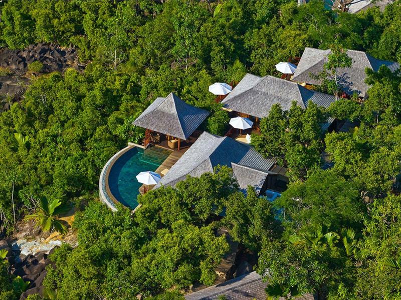 Vue aérienne d'une villa de villégiature isolée entourée de verdure dense avec une piscine incurvée.