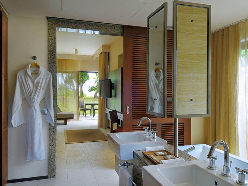 Salle de bain d'hôtel moderne avec double vasque, peignoirs et vue sur la chambre.