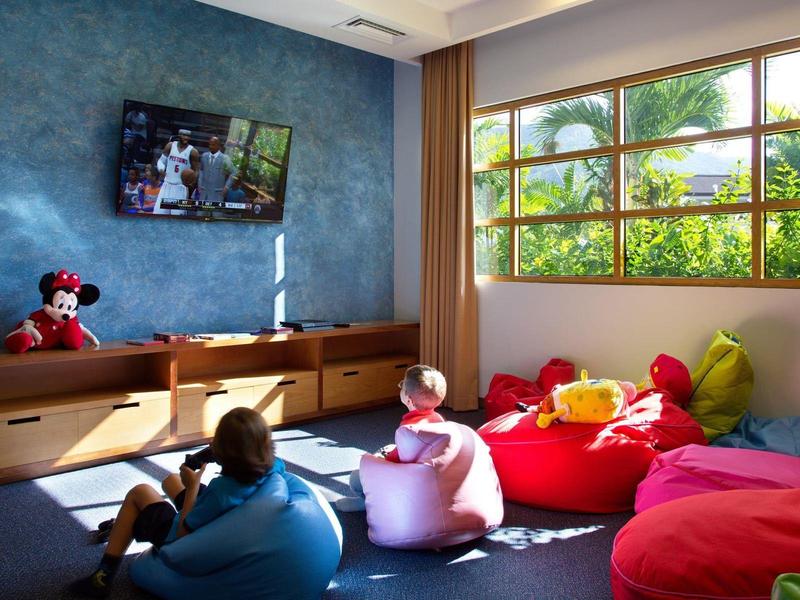 Kinderzimmer mit bunten Sitzsäcken, großem Fenster und Fernseher an blauer Wand.