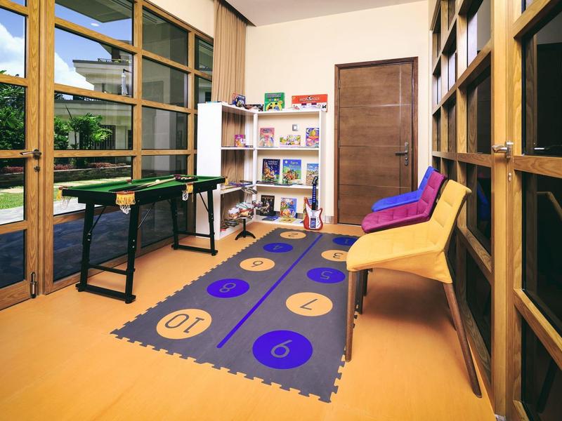 Heller Raum mit Holztüren, buntem Spielteppich, Regalen und farbenfrohen Stühlen an der Wand.