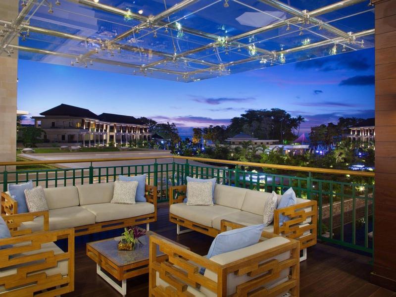 Terrasse mit weißen Polstersofas und Holzmöbeln bei Abenddämmerung, Blick auf Nachbargebäude.