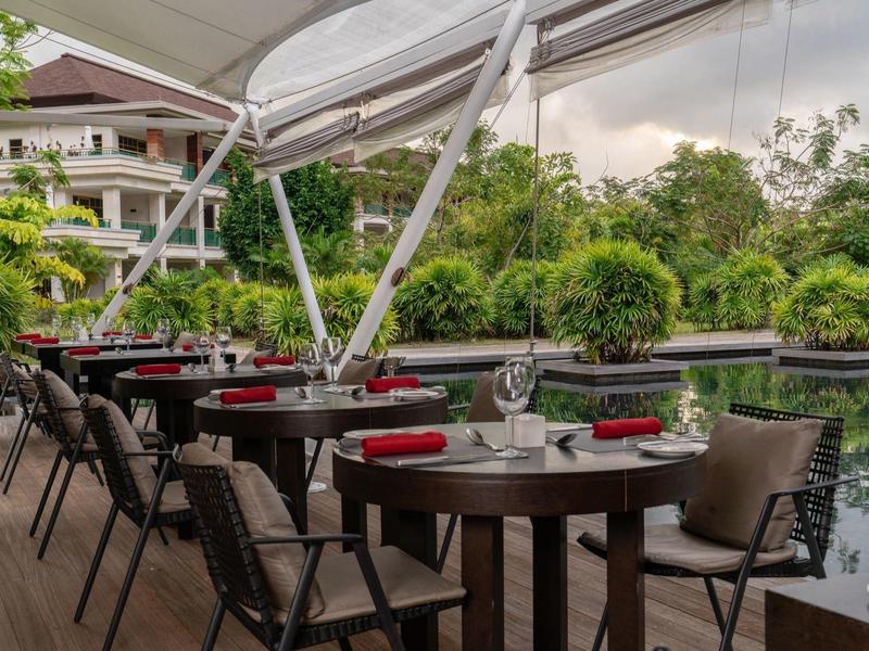 Freiluftrestaurant mit Holztischen, schwarzen Stühlen und Blick auf einen ruhigen Fluss und grüne Bäume.