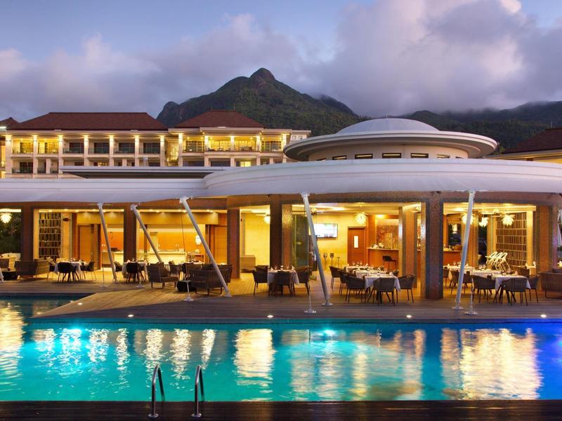 Luxushotel bei Dämmerung mit beleuchtetem Pool und Bergen im Hintergrund.