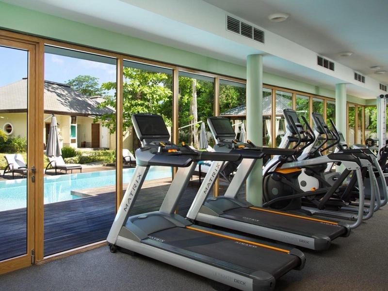 Fitnessraum mit Laufbändern und Blick durch große Fenster auf einen Pool und Garten.