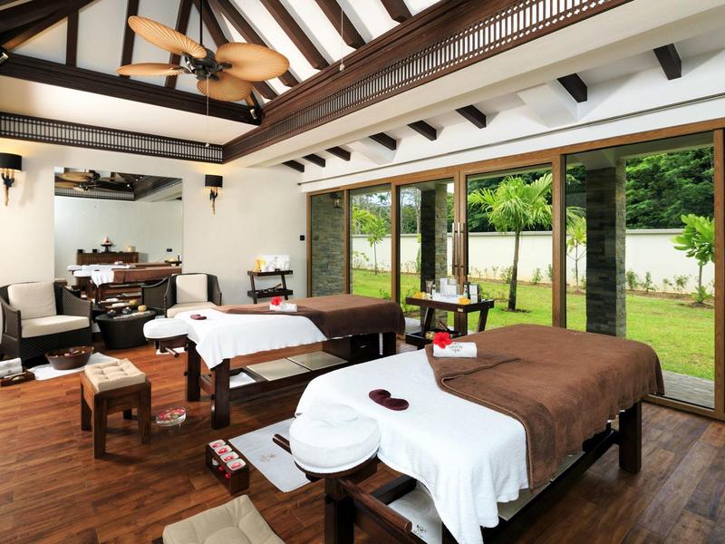 Helles Spa-Zimmer mit Holzböden, zwei Massageliegen und großer Glasfront zum Garten.