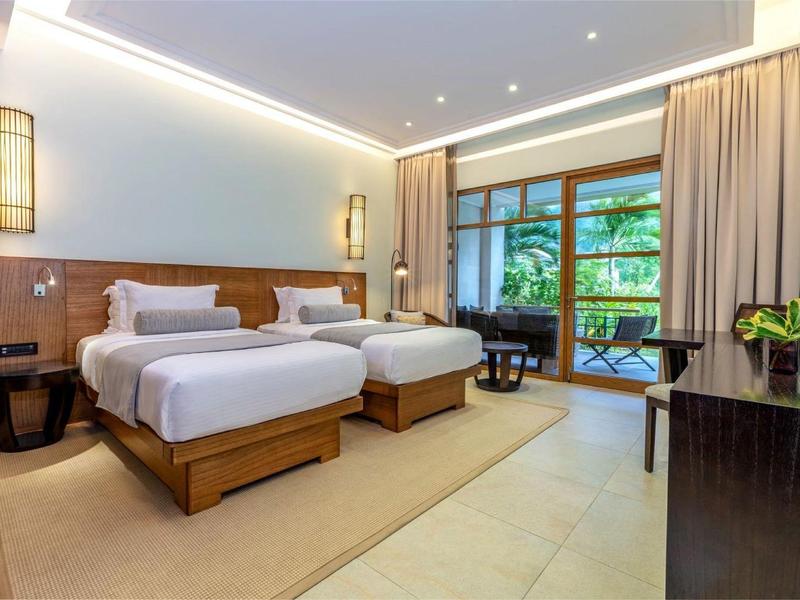 Modernes Hotelzimmer mit zwei Betten, Holz- und Beigetönen, großer Fensterfront und Balkon.