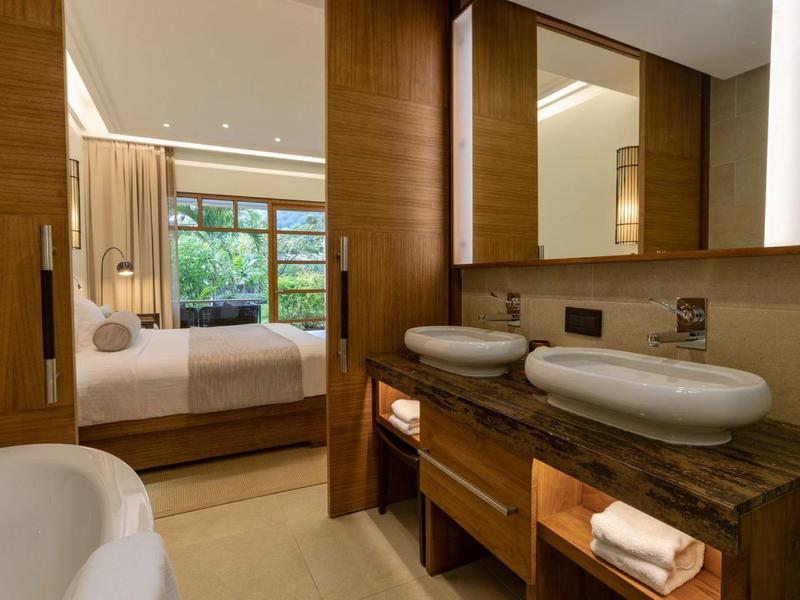 Modernes Badezimmer mit Doppelwaschbecken, Holzfronten und Blick ins angrenzende Schlafzimmer.