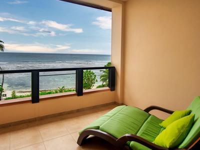 Balcón con silla reclinable verde y vista al mar bajo un cielo azul con nubes.