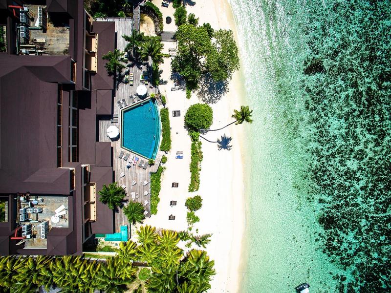 Vista aérea de un resort con piscina, playa de arena blanca y agua turquesa.