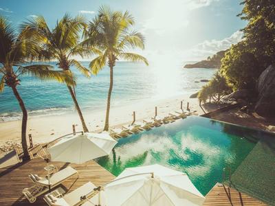 Coucher de soleil sur une piscine avec parasols, chaises longues et palmiers sur la plage.