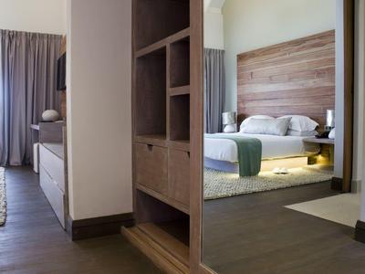 Moderní část hotelového pokoje se postelí, nočním stolkem a dřevěnou skříní.