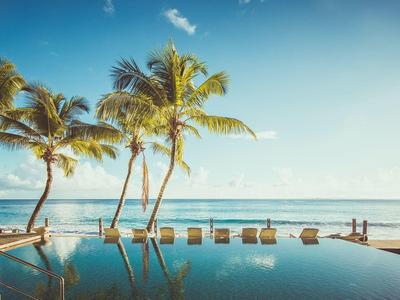 Infinity-Pool mit reflektierendem Wasser, Palmen und klarem Himmel am tropischen Strand.