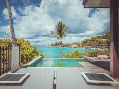 Infinity bazén s výhledem na moře a tropickou krajinu pod zataženou oblohou.