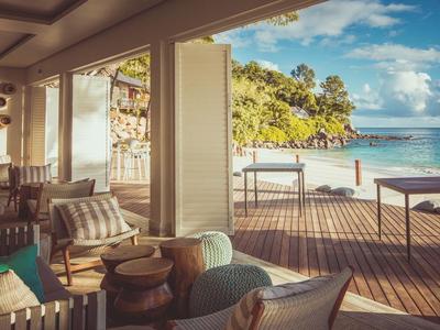 Lounge de plage confortable avec fauteuils et tables, vue sur la mer et le ciel.