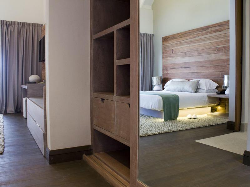 Moderní část hotelového pokoje se postelí, nočním stolkem a dřevěnou skříní.