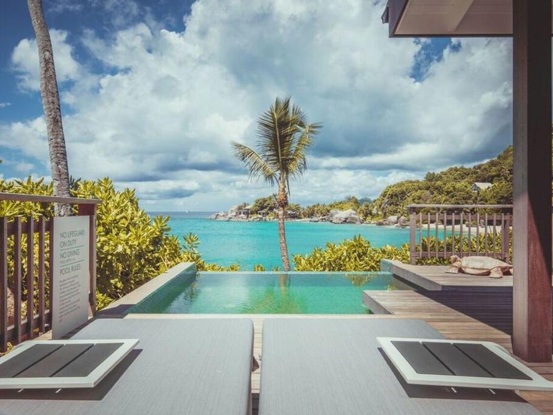 Infinity bazén s výhledem na moře a tropickou krajinu pod zataženou oblohou.