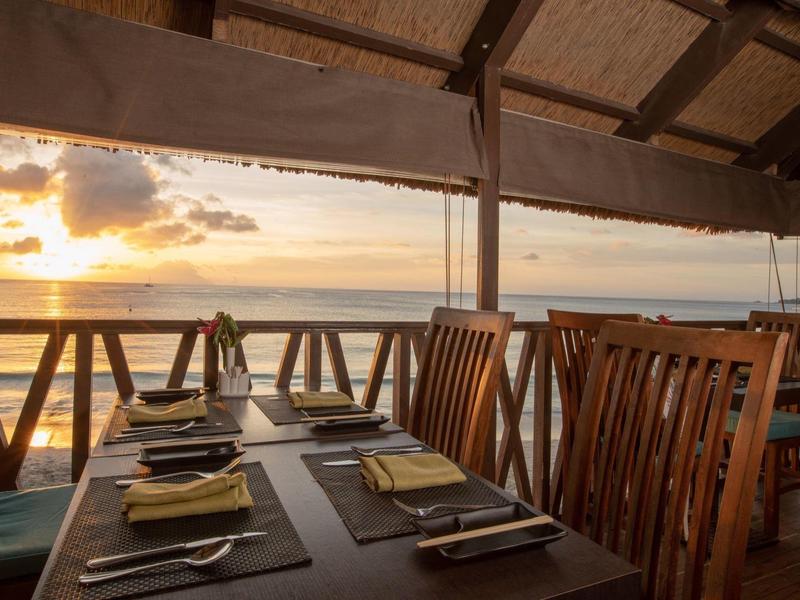 Restaurante con muebles de madera, mesa puesta en terraza cubierta con vista al atardecer sobre el agua.