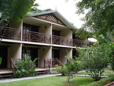 Twee verdiepingen tellend hotelgebouw met balkons omgeven door weelderig groen en grote bomen.