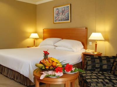 Gezellige hotelkamer met groot bed, fruitschaal op tafel en een fauteuil met patroon.