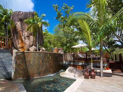 Außenpool mit Wasserfall und Sitzbereich umgeben von Palmen und Sonnenschirmen.