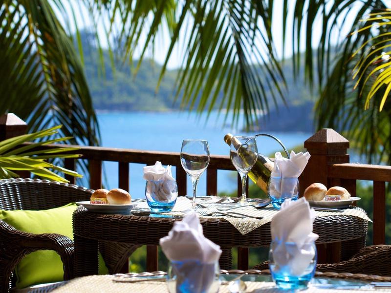Una terrazza accogliente con tavolo apparecchiato, circondata da palme con vista sull'acqua.
