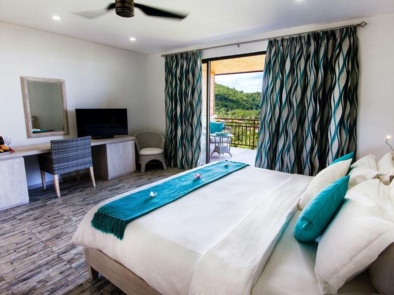 Camera d'hotel luminosa con letto matrimoniale, scrivania e porte su balcone con vista sul verde.