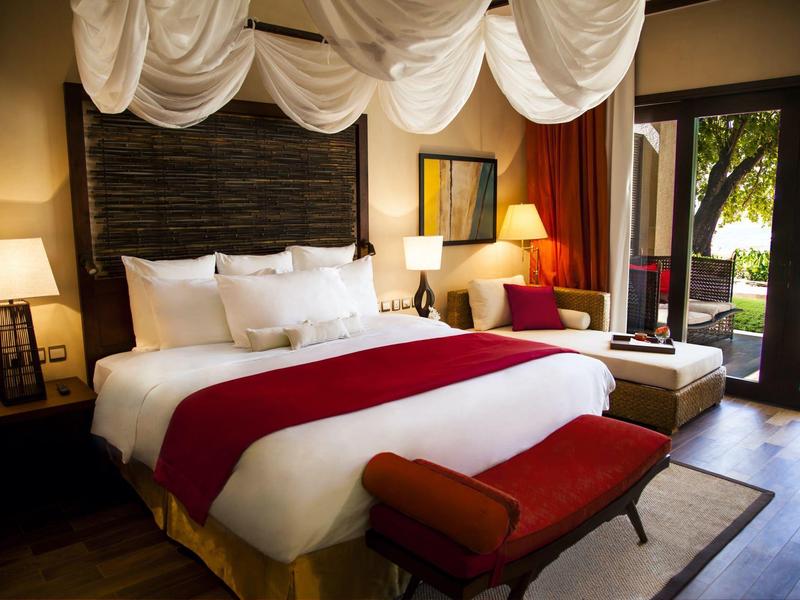 Gemütliches Schlafzimmer mit großem Bett, rotem Überwurf, dunklem Holzboden und Blick auf Garten.